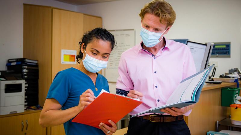 A consultant and nurse checking test results of a patient, both wearing face masks