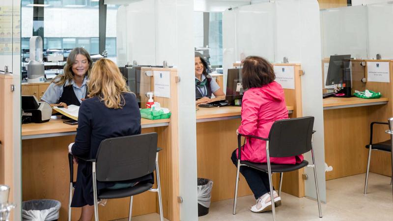 Outpatients filling out a form handed to them by a worker at the other side of the desk.