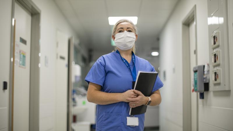 Healthcare worker wearing a face covering and holding a chart.