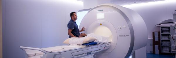 A doctor adjusting the dials on a MRI machine as a patient lays on the bed